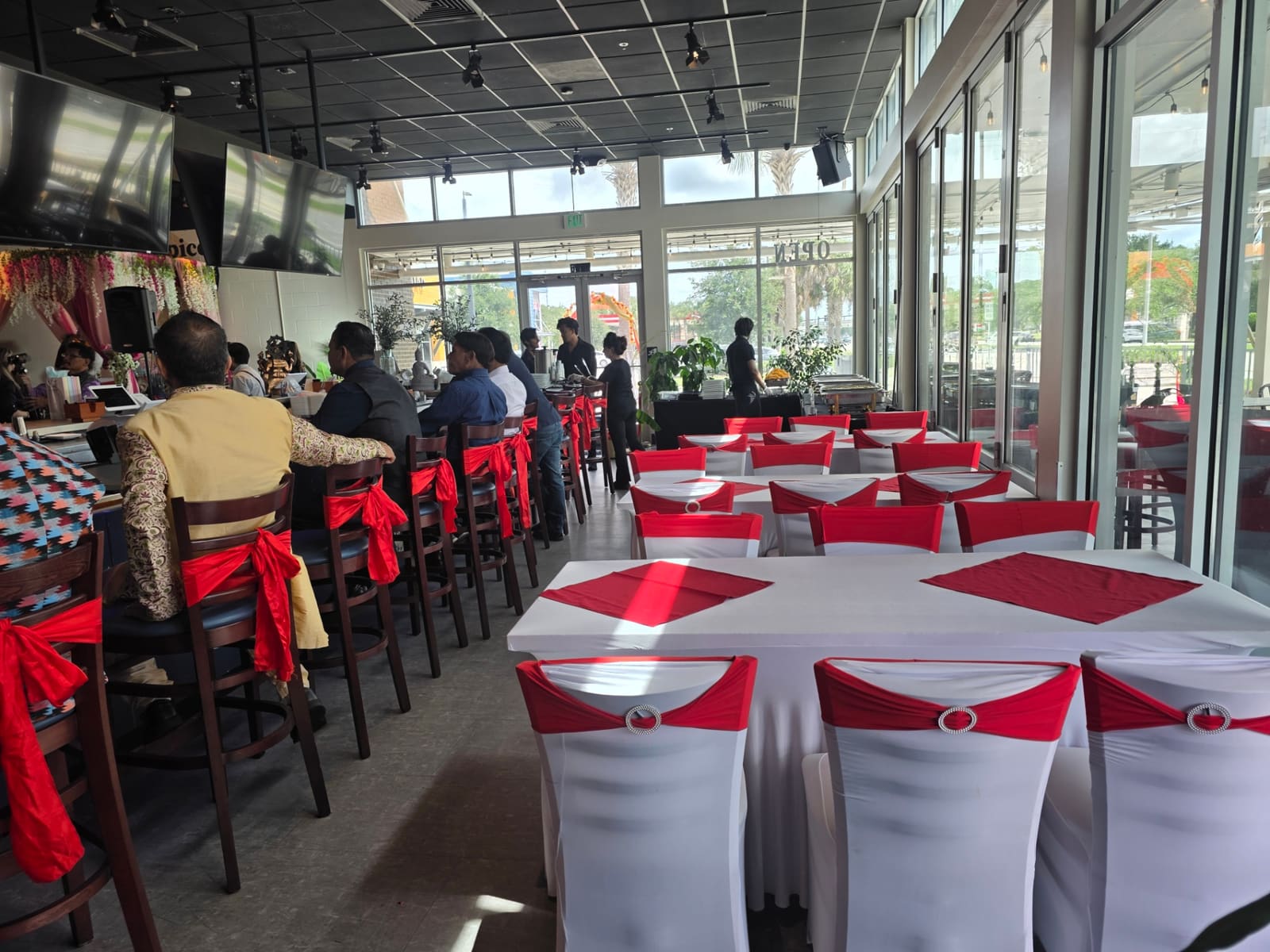 Dining tables dressed in white linens with red chair sashes for a wedding reception